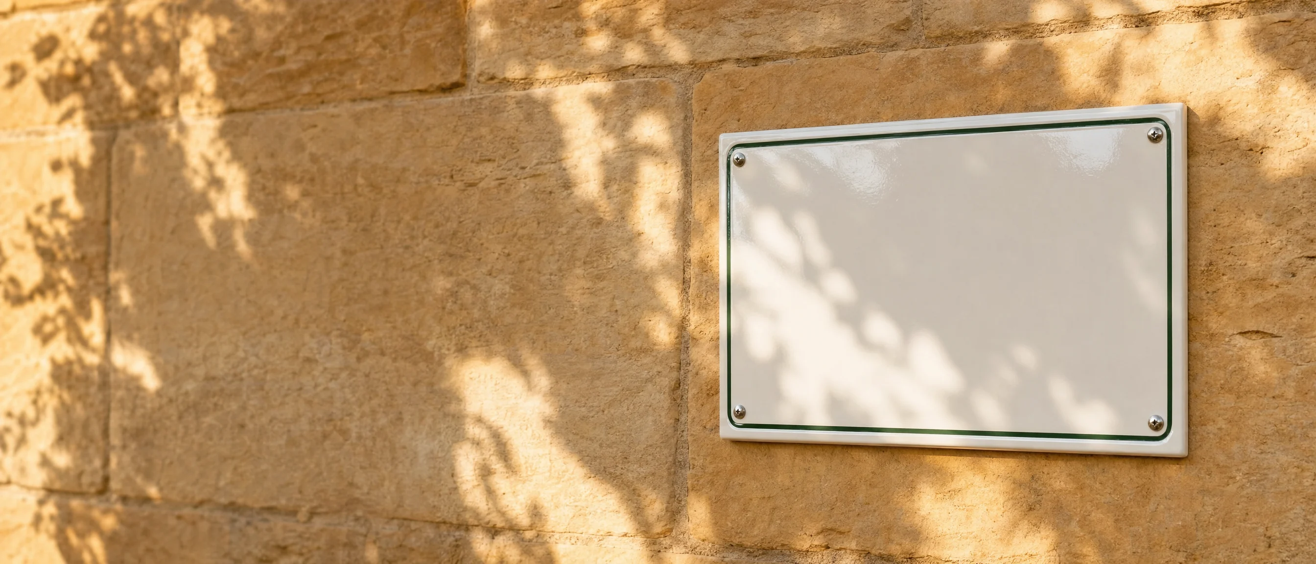 Weißes Emailschild ohne Aufschrift an einer Sandsteinwand im Sonnenlicht